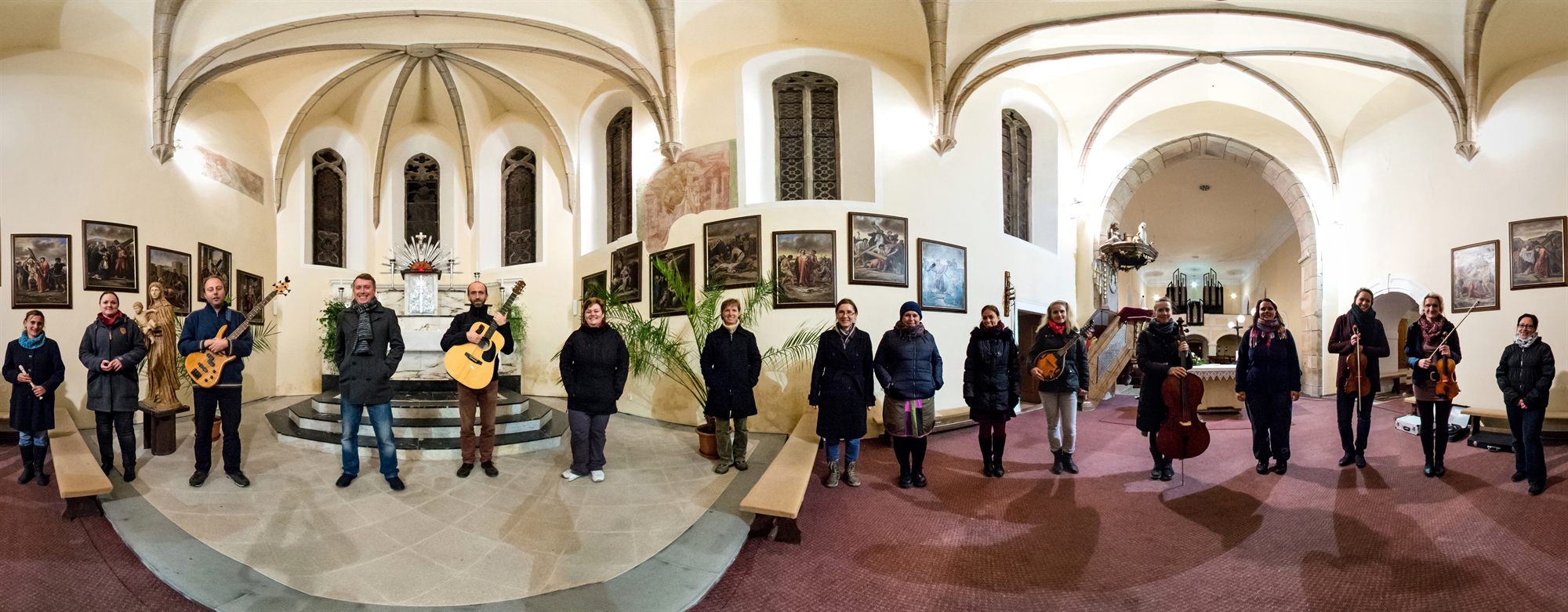 Panoramatická fotografie členů skupiny Labyrint s hudebními nástroji v interiéru kostela